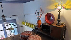 A cozy seating area with two patterned ottomans on a wooden deck, a decorative lamp, and a vase with branches.