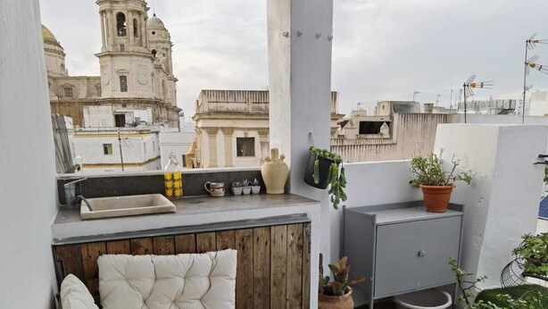 A rooftop terrace with a cushioned seating area, a small table, and potted plants.
