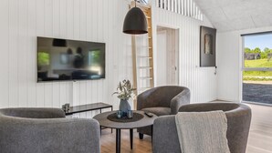 Ein modernes Wohnzimmer mit Flachbildfernseher, grau gepolsterten Möbeln, einem runden Couchtisch und einer Pendelleuchte.