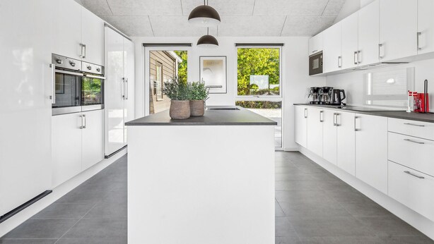Eine moderne Küche mit weißen Schränken, einer zentralen Kochinsel mit Blumentopf und einer Kaffeestation.