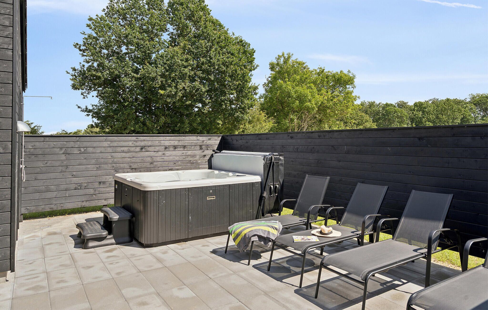 An outdoor patio with a hot tub, lounge chairs, and a wooden fence.