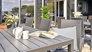Eine Terrasse im Freien mit Korbmöbeln, einem Tisch mit einem Buch, einer Blumenvase und einem Blumentopf.