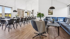 Ein geräumiger Raum mit einem langen Esstisch, mehreren Stühlen, einem Sofa und einer großen Topfpflanze.