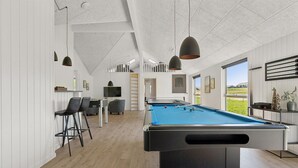 Ein Billardtisch in einem Raum mit Holzboden, weißen Wänden und einem großen Fenster mit Blick ins Freie.
