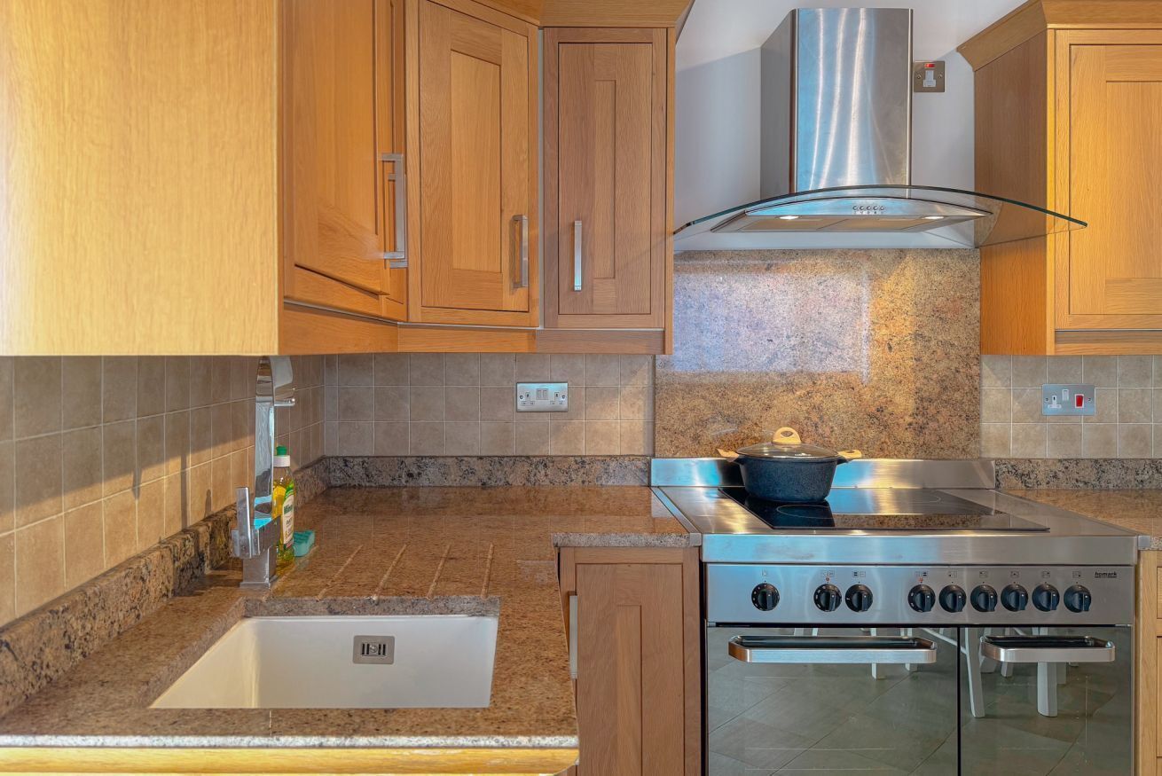 A kitchen with wooden cabinets, a stainless steel range hood, a built-in oven, and a granite countertop.