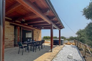 Un espace extérieur abrité, aménagé pour les repas, avec un mur en briques, une table et des chaises, ainsi qu’un jacuzzi.