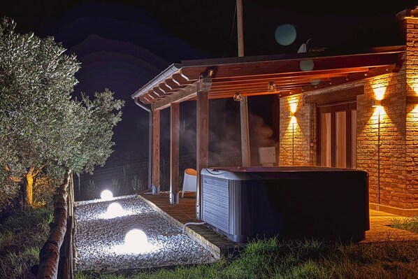Un bain à remous situé à l’extérieur d’un bâtiment à la façade en pierre et agrémenté d’une pergola en bois.
