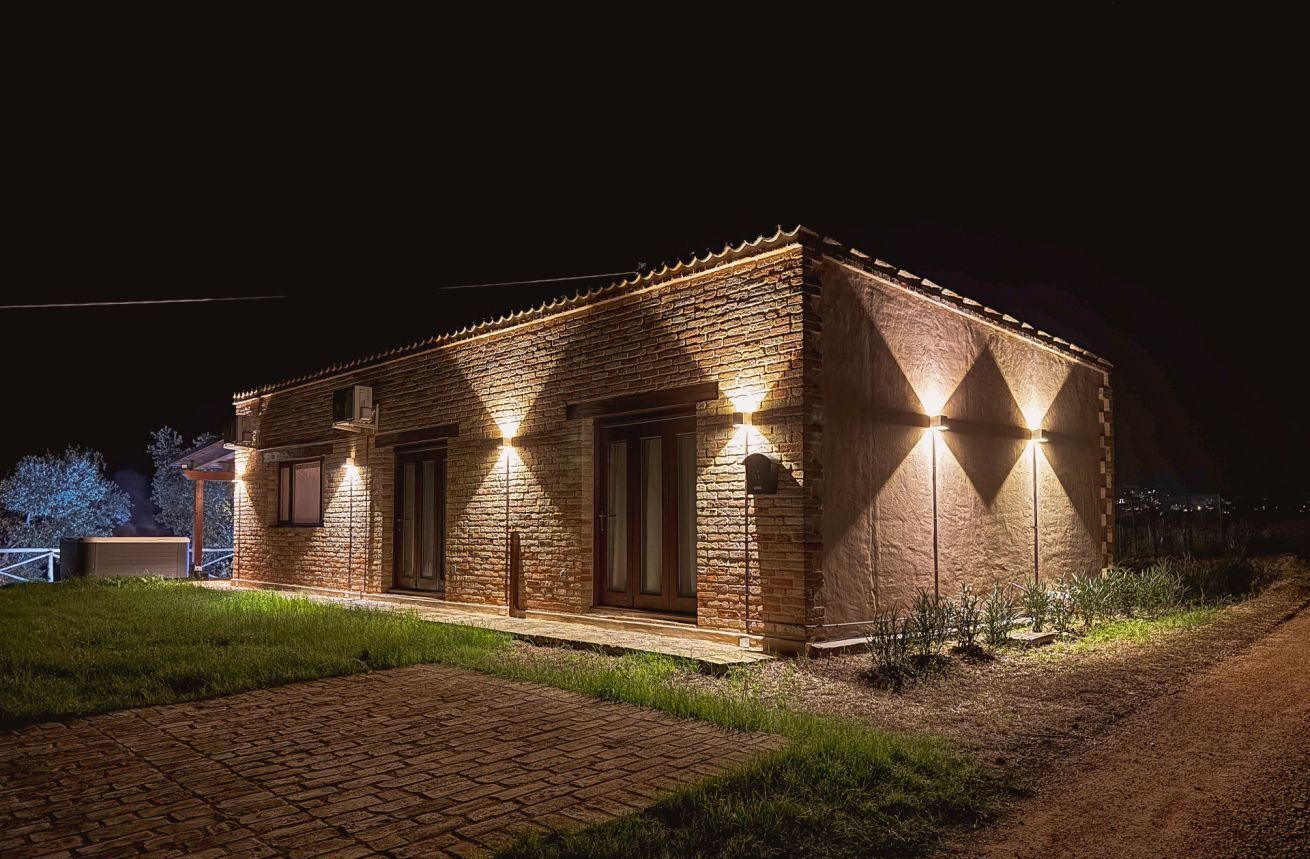 A brick building with a flat roof, illuminated by exterior lights, a paved entrance, and a grassy area in front.