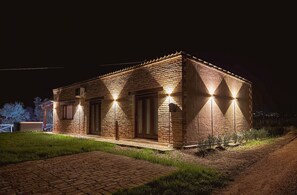 Un bâtiment en briques, doté d’un toit plat, éclairé par des lampes extérieures, avec une entrée pavée et une pelouse devant.