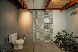 A bathroom with a toilet, shower, and a tiled wall with a geometric pattern. - Villa Karar (Ubud)