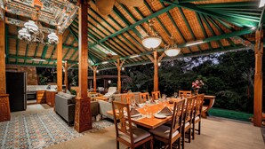 Un'area pranzo all'aperto con tetto di paglia, mobili in legno e vista sul verde circostante.
