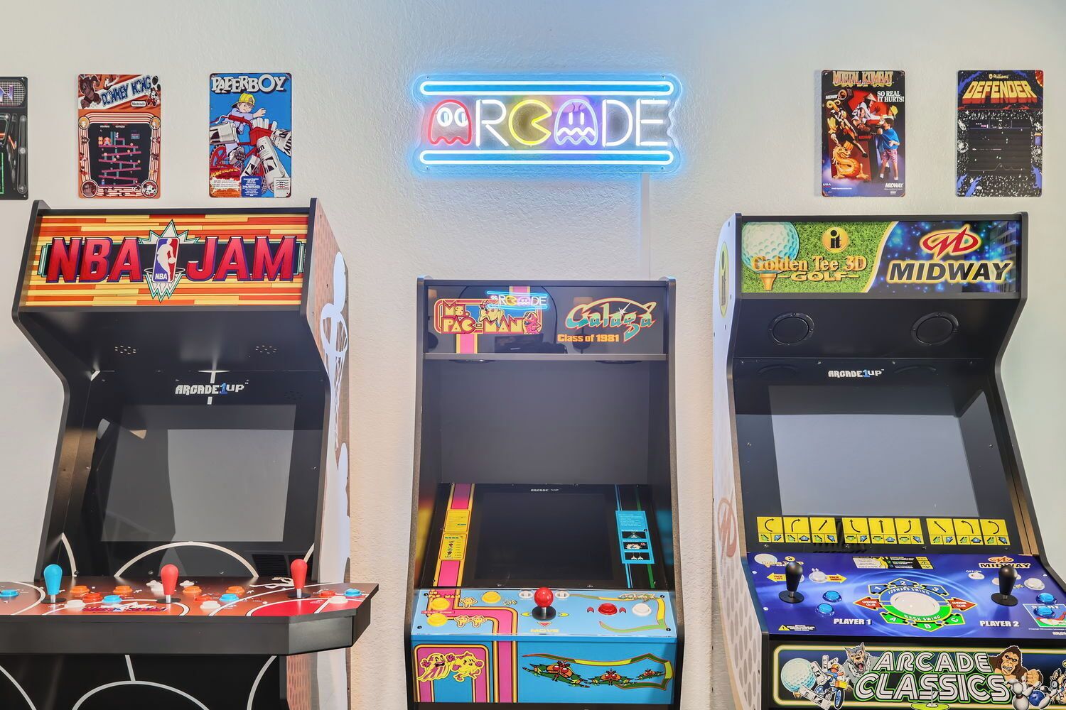 Três máquinas de fliperama com títulos e logotipos visíveis, um letreiro de neon acima e uma exibição de caixas de jogos na parede.