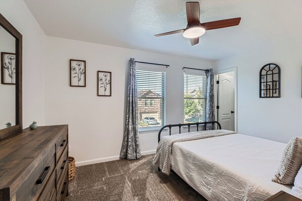 A bedroom with a bed, a dresser, a ceiling fan, and a window with blinds.