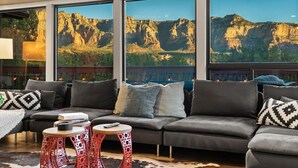 Un soggiorno moderno con un divano grigio, cuscini decorati e vista su un paesaggio montuoso attraverso ampie finestre.
