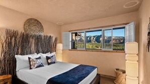 Una camera da letto con un letto, una finestra con persiane, un elemento decorativo a parete e vista sulle montagne.