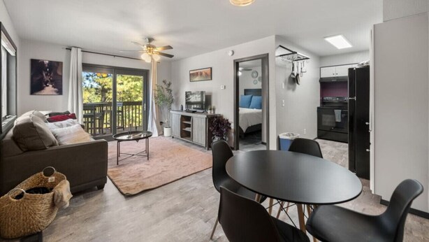 A modern living room with a sofa, coffee table, and dining area. There is a balcony with a view of trees. The kitchen is visible through an open door. - Pet Friendly Flagstaff home Mountain Views &Grill (Flagstaff)