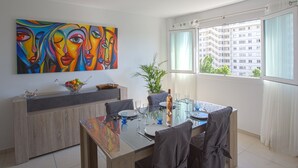 A dining area with a modern table set for four, a colorful abstract painting on the wall, and a view of a building through a window. - Apartment L'Onyx by Interhome (Toulon)