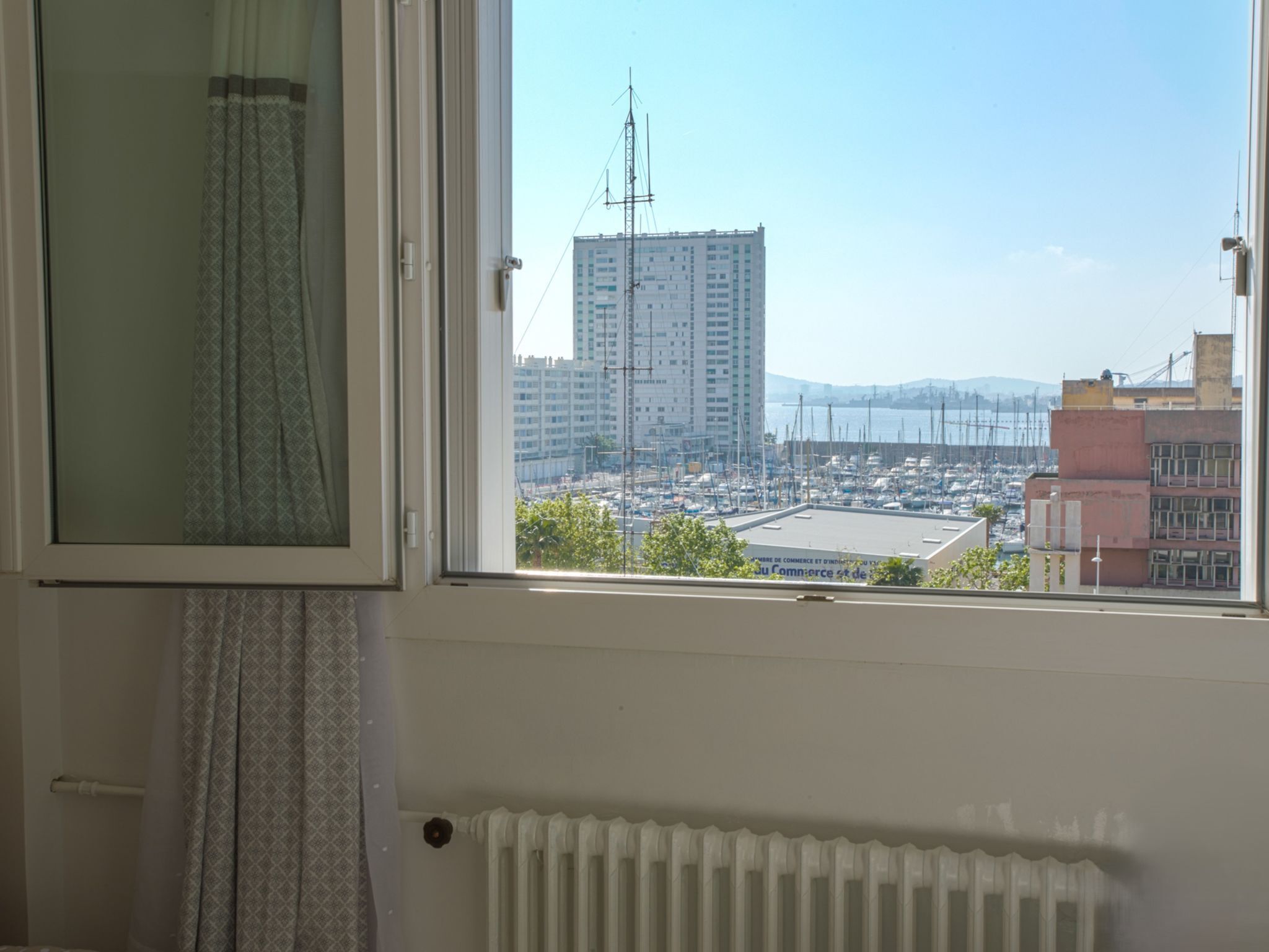 Une chambre avec une fenêtre donnant sur un port de plaisance et des immeubles.