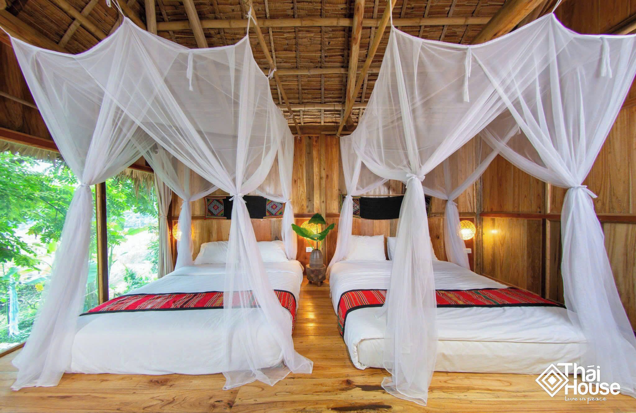 A room with two beds, each covered with white mosquito netting and red and black patterned bedding.