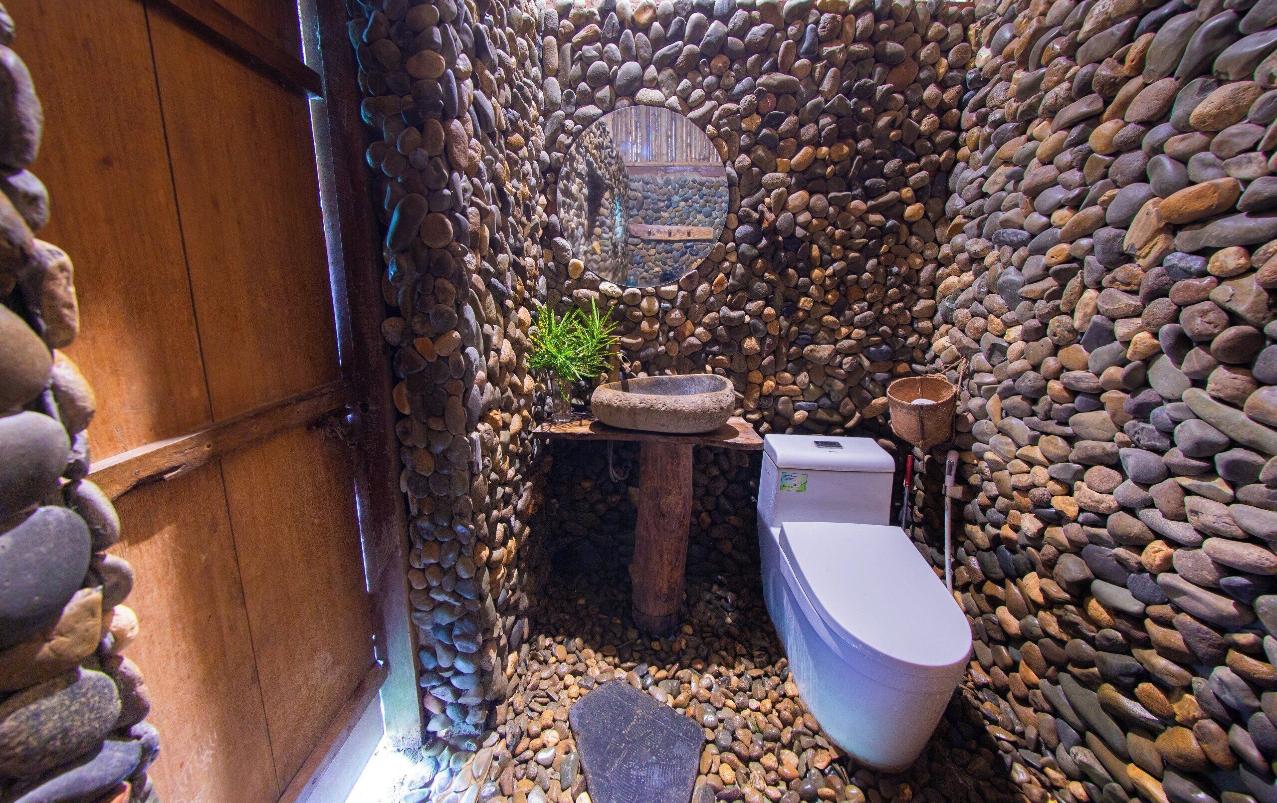 Une salle de bain rustique avec un mur en pierre, une porte en bois, un lavabo en pierre et des toilettes blanches.