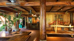 A rustic wooden interior with a pool table, wooden benches, and a large potted plant. - Thai House Pu Luong (Co Lung)