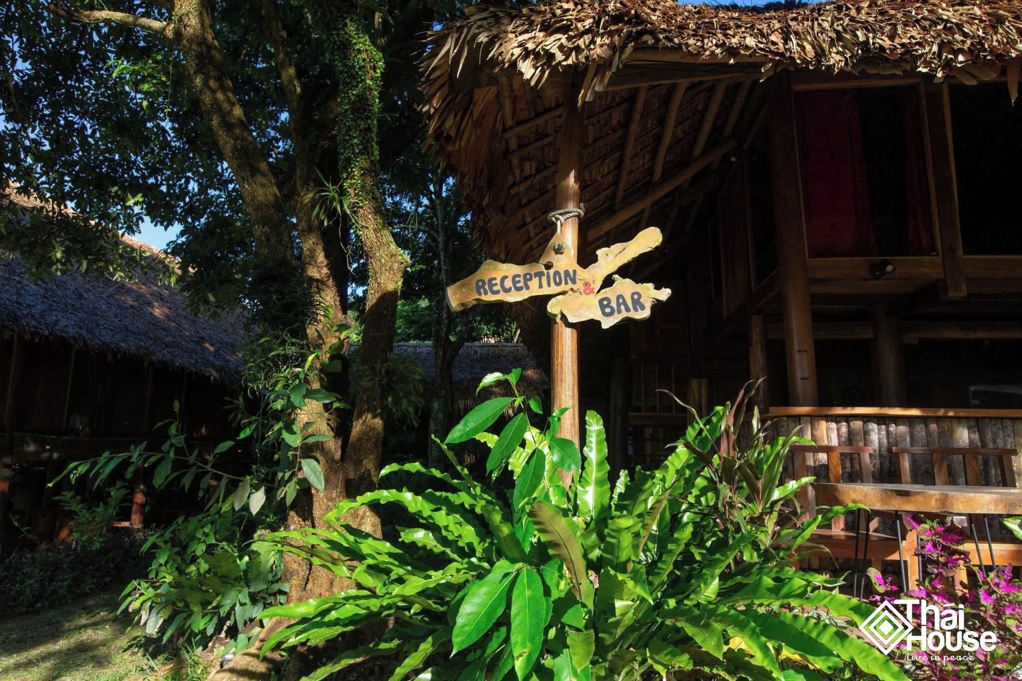 A wooden reception and bar signpost with a thatched roof structure in the background.
