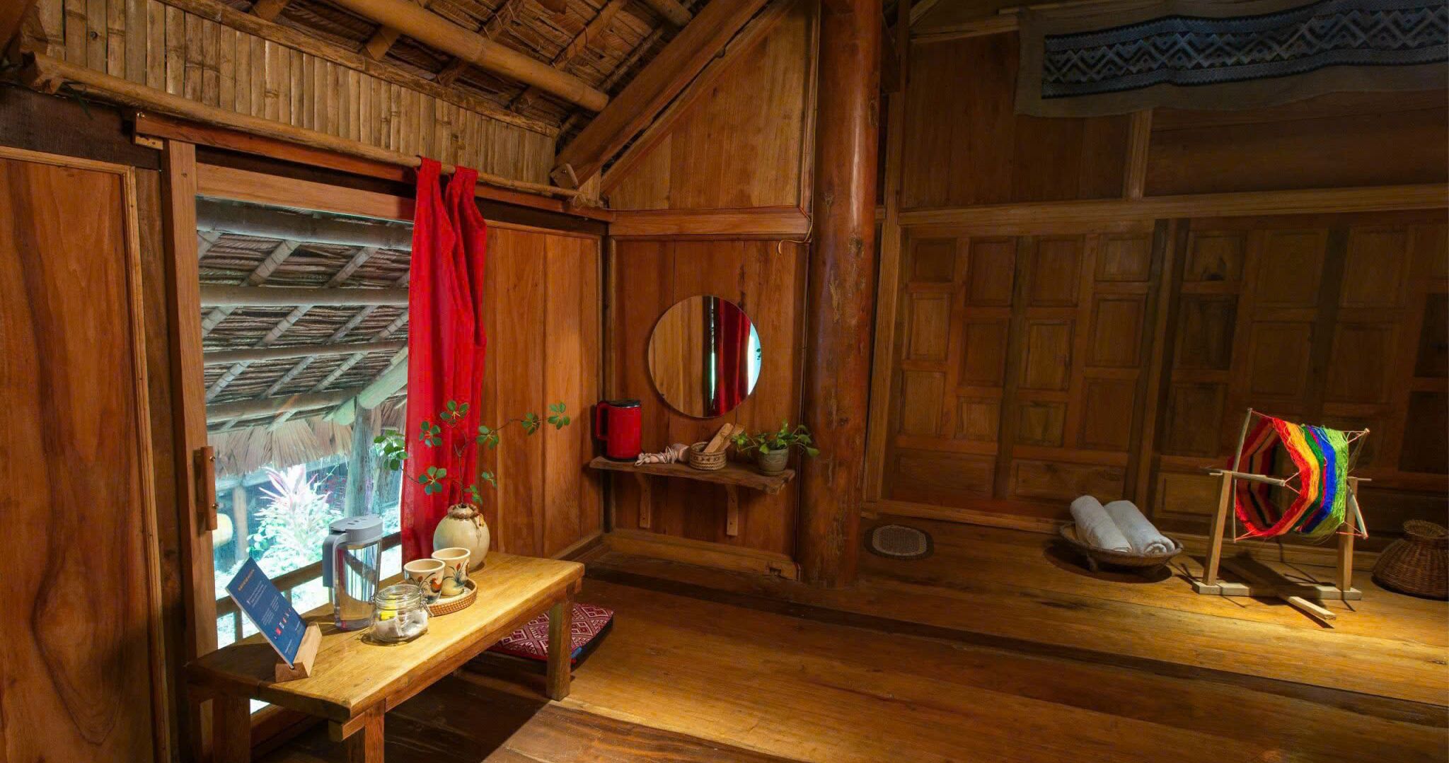 Une pièce rustique avec des murs en bois, une table en bois, un rideau rouge, un miroir et un objet tissé aux couleurs vives, posé sur un présentoir.
