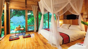A room with a wooden floor, a bed with white bedding, a canopy bed, and a view of greenery outside. - Thai House Pu Luong (Co Lung)