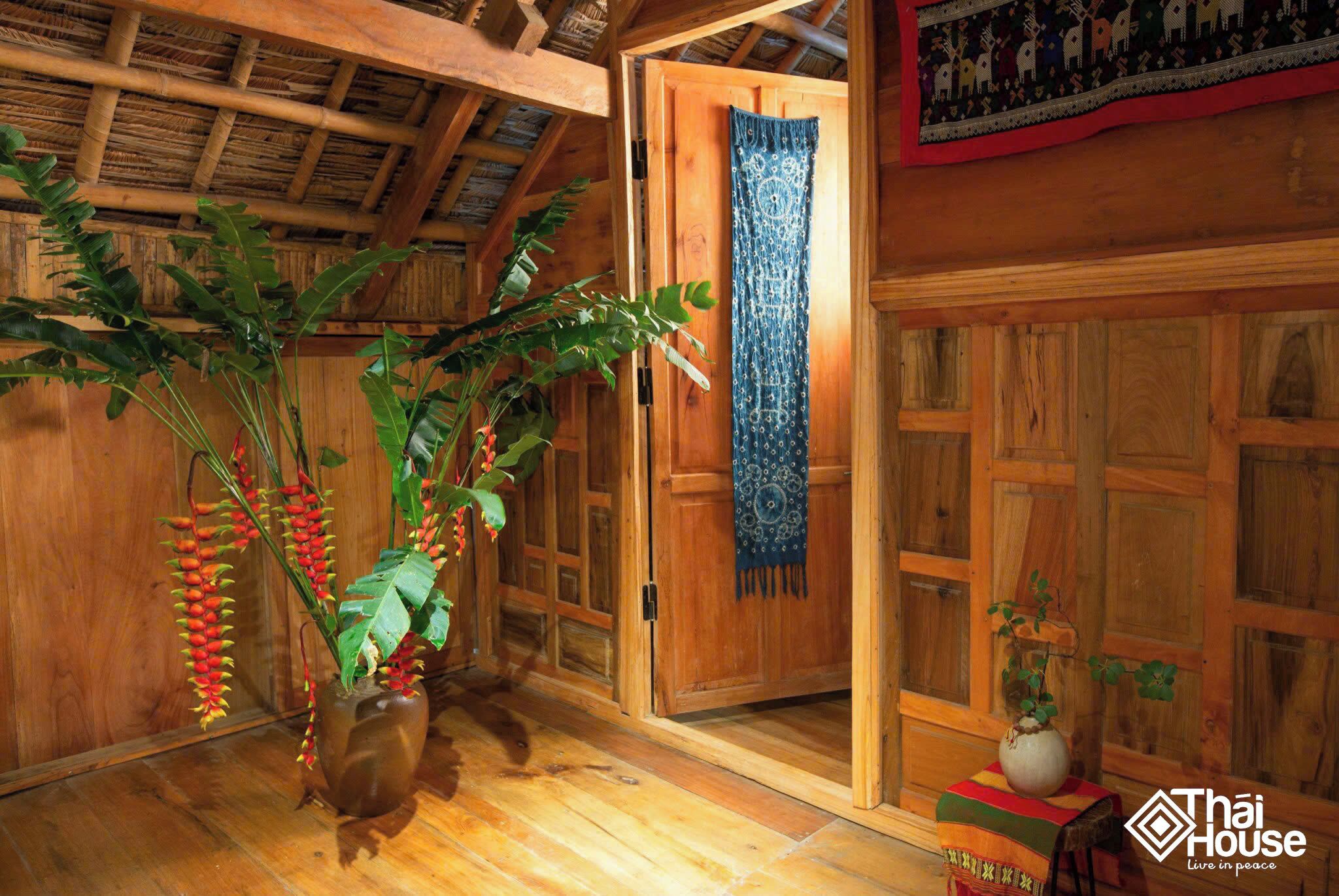 A wooden room with a door, a blue patterned curtain, and a plant in a vase.