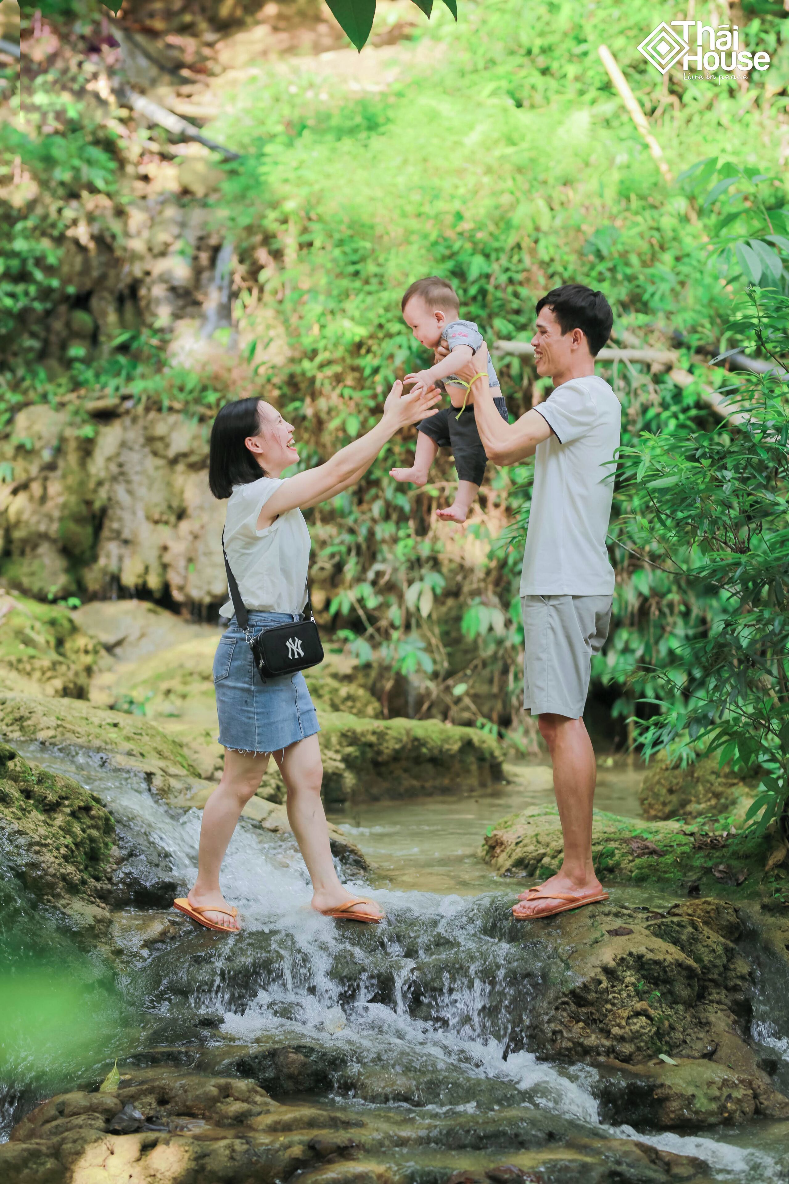 A family taking a photo by a small waterfall in a lush, green environment.