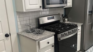 Uma cozinha com armários brancos, fogão de aço inoxidável, micro-ondas e geladeira.