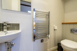 A bathroom with a white sink, a chrome towel rack, a toilet, and a mirror.