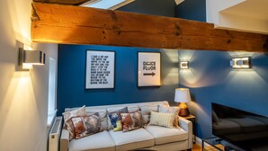 Un salon moderne avec un plafond haut, un canapé agrémenté de coussins à motifs, un téléviseur fixé au mur et des panneaux de signalisation.