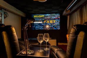A cinema room with leather recliner seats, a screen displaying a film, and two glasses on a tray.