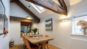 Un espace repas avec une table en bois, des chaises orange, un lustre et une lucarne.