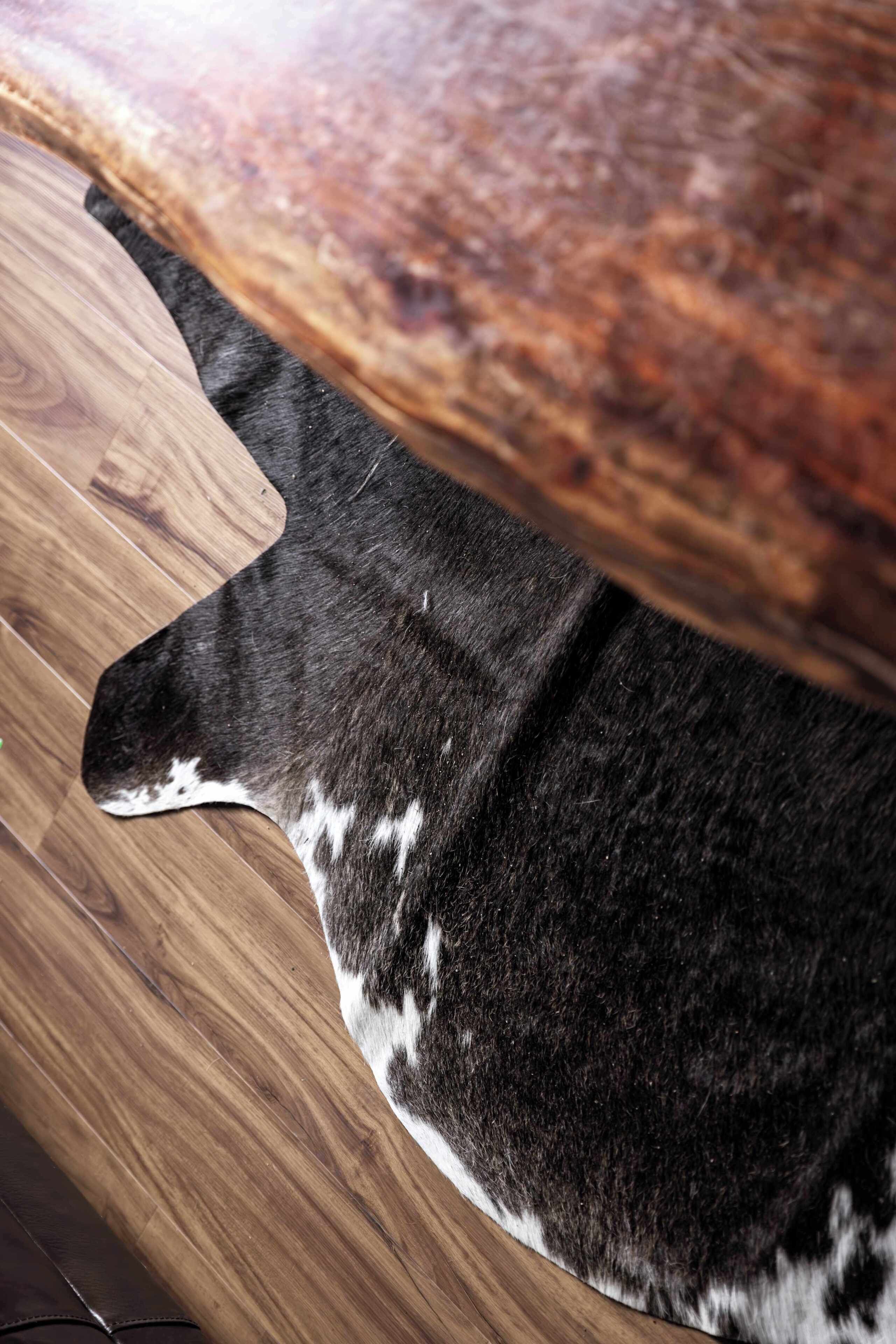 Parte de un piso de madera con un tapete oscuro y estampado que lo cubre parcialmente.
