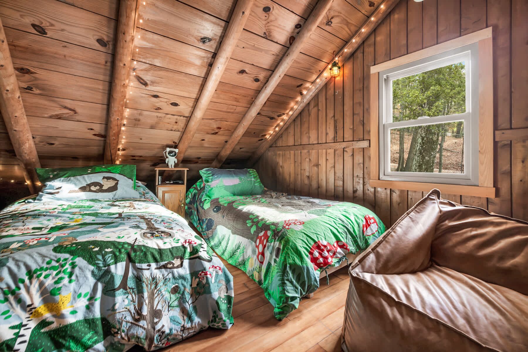 Un dormitorio acogedor en el ático con dos camas, una ventana y techo de madera.