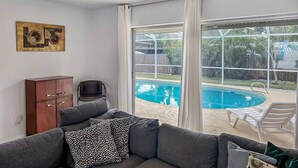 Un salon avec un canapé gris, un meuble en bois et une grande fenêtre donnant sur une piscine.