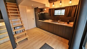 Una cocina compacta con suelo de madera, horno empotrado, fregadero e iluminación colgante.