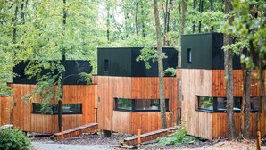 Una hilera de cabañas de madera con techos negros, ubicadas en una zona boscosa.