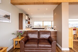 A modern living room with a leather sofa, a wooden coffee table, and a kitchen in the background.