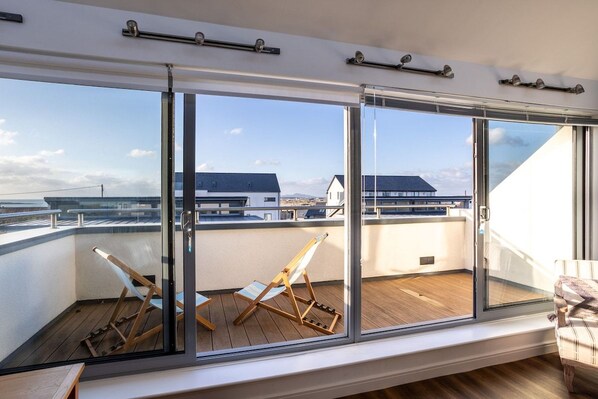 Top floor sea view balcony with full-length sliding glass doors and deck chairs, upside-down pet-friendly holiday home sleeping eight in Rhosneigr, Anglesey