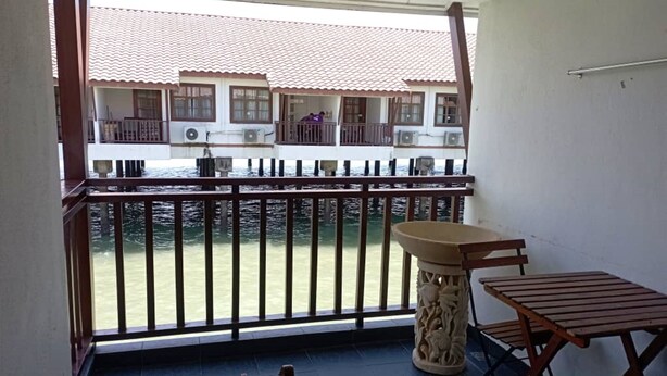 A balcony with a view of a building with a tiled roof. There is a table and two chairs on the balcony. - Alpine Premium Water Chalet 2  (Port Dickson)
