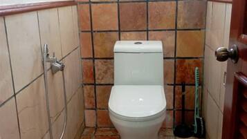 A small bathroom with a toilet, a shower, and a broom.