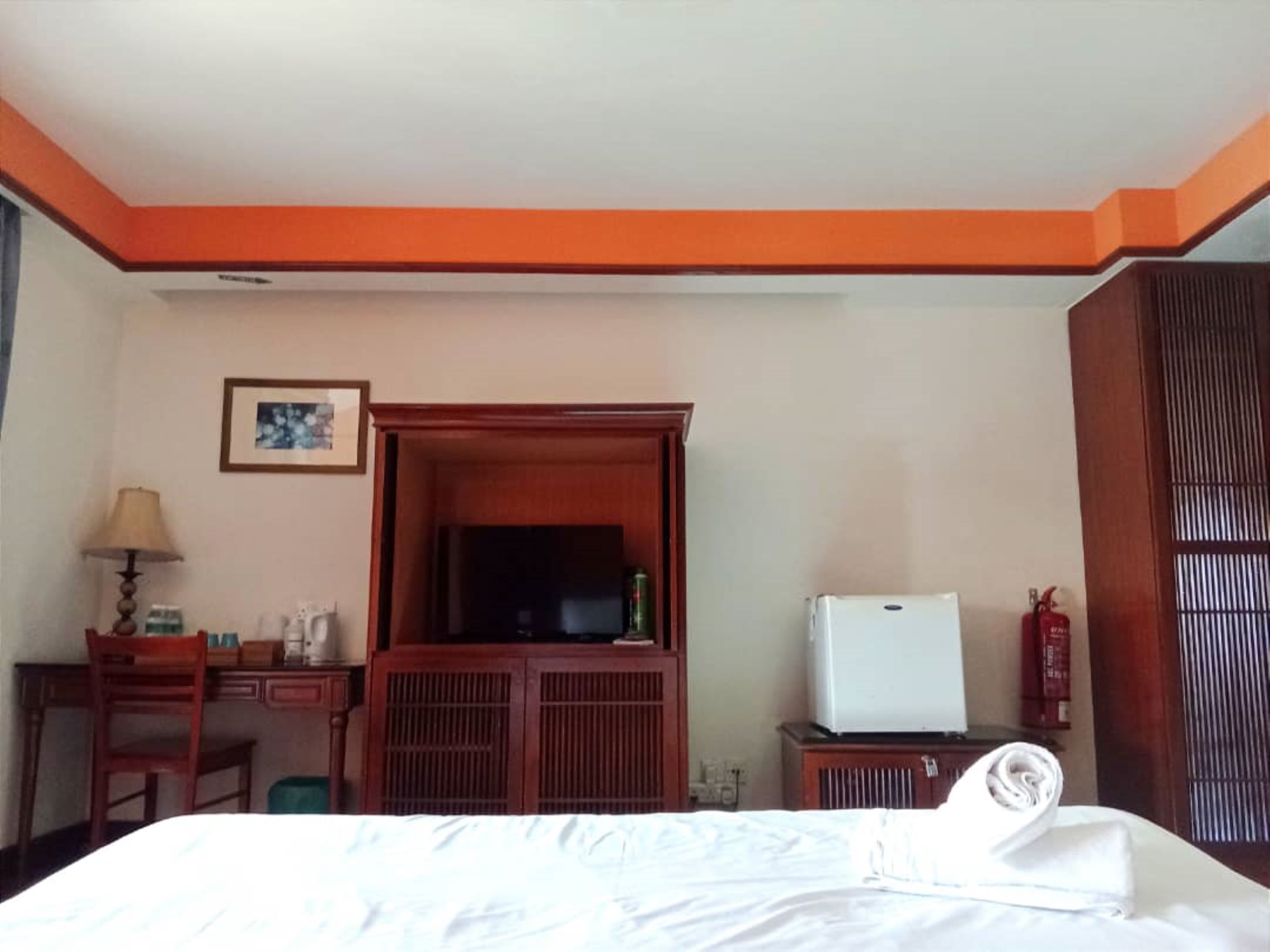 A hotel room with a bed, a desk with a lamp, a television, and a wardrobe.
