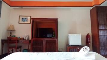 A hotel room with a bed, a desk with a lamp, a television, and a wardrobe.