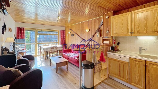 Un intérieur chaleureux avec un plancher en bois, un coin repas, un canapé et une cuisine dotée de meubles en bois.