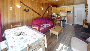 L’intérieur d’un chalet accueillant, avec un plafond en bois, une table à manger recouverte d’une nappe à motifs floraux, un canapé rouge et un coin cuisine doté de meubles en bois.