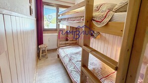 Une petite pièce avec des lits superposés en bois, une fenêtre donnant sur un paysage et un radiateur.