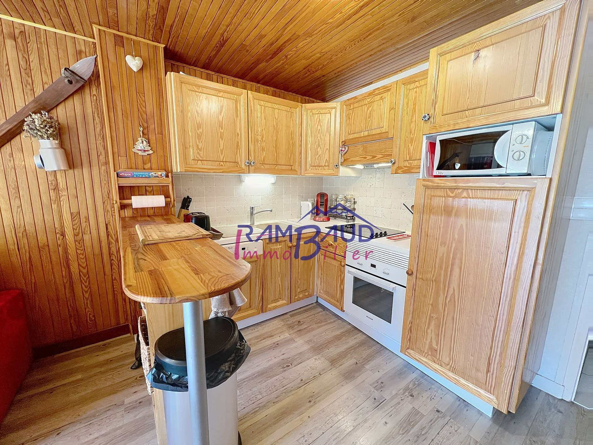 A kitchen with wooden cabinets, a microwave, a stove, and a trash can.